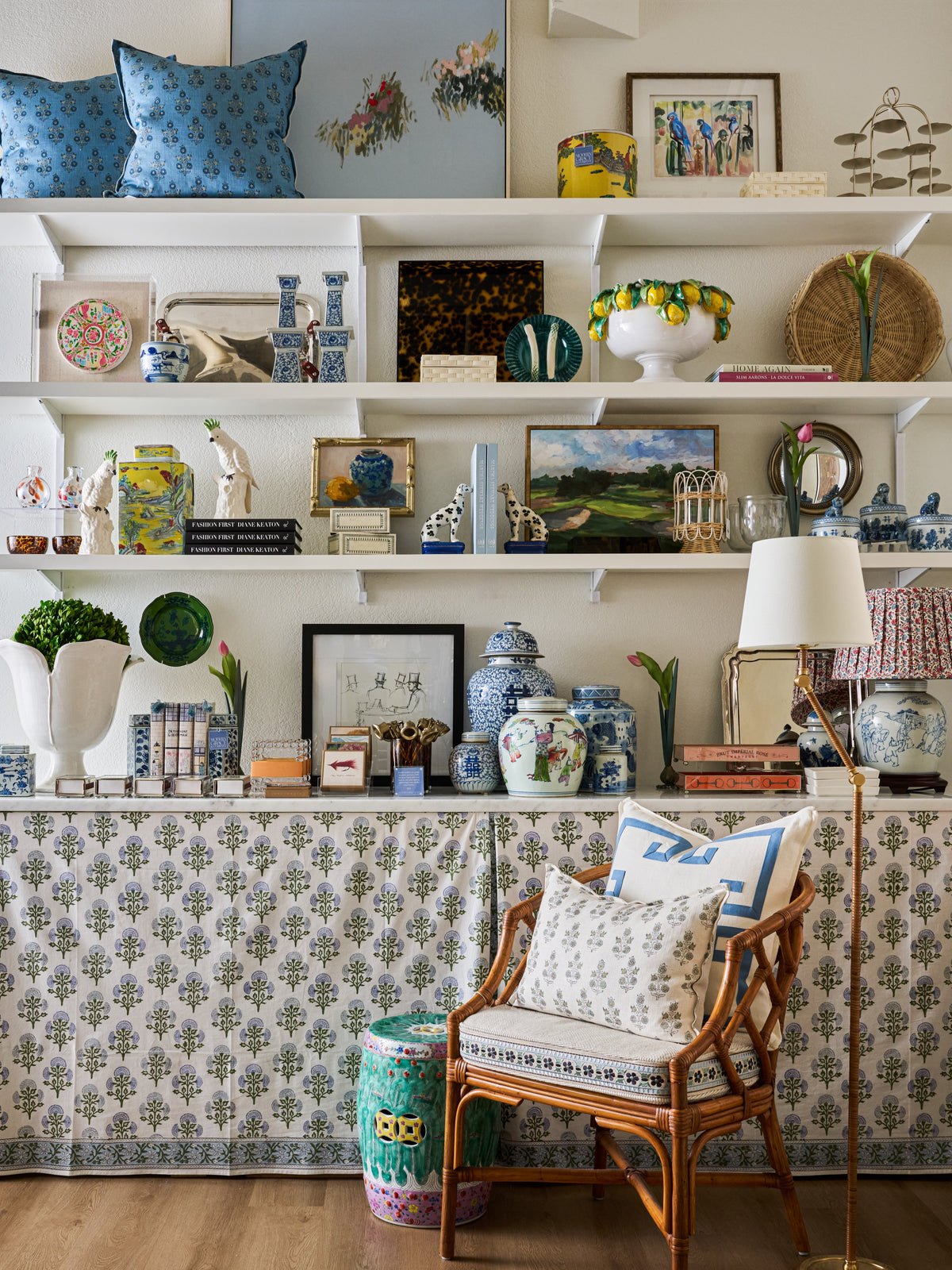 Collected ceramics, artwork and accessories on styled shelves beside a woven chair.